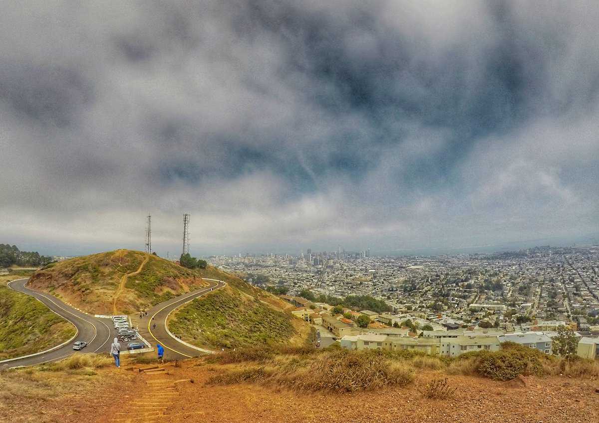 what to do in San Francisco in one day - Twin Peaks summit A scenic view from Twin Peaks in San Francisco, showing a winding road, two radio towers, and the vast cityscape under a cloudy sky.