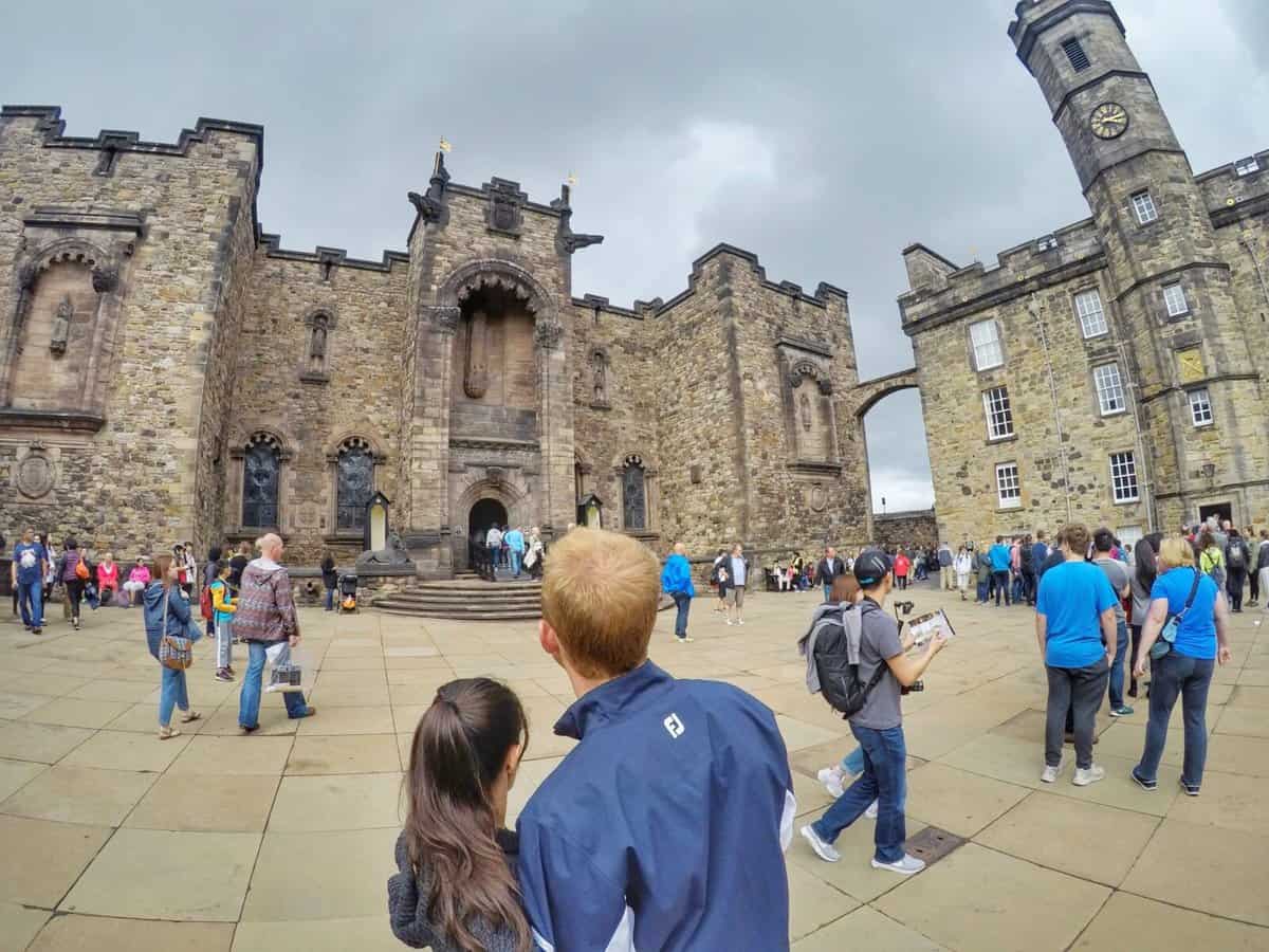 Tourists gathered in front of the historic Edinburgh Castle in Edinburgh, Scotland, with its stone walls and towers under a cloudy sky.