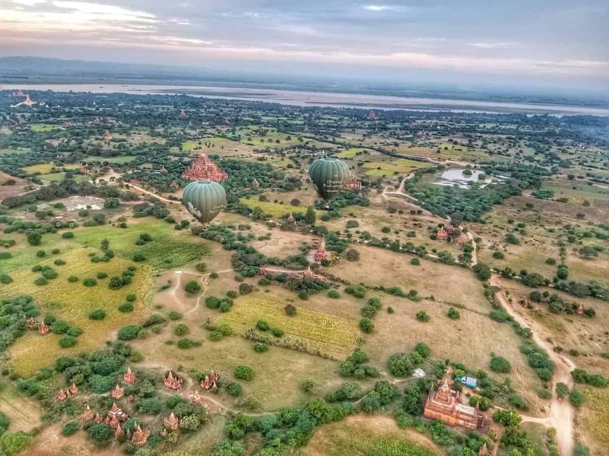 Arial view of Bagan, Myanmar featuring hot air balloons floating over a landscape dotted with ancient temples and surrounding greenery.
