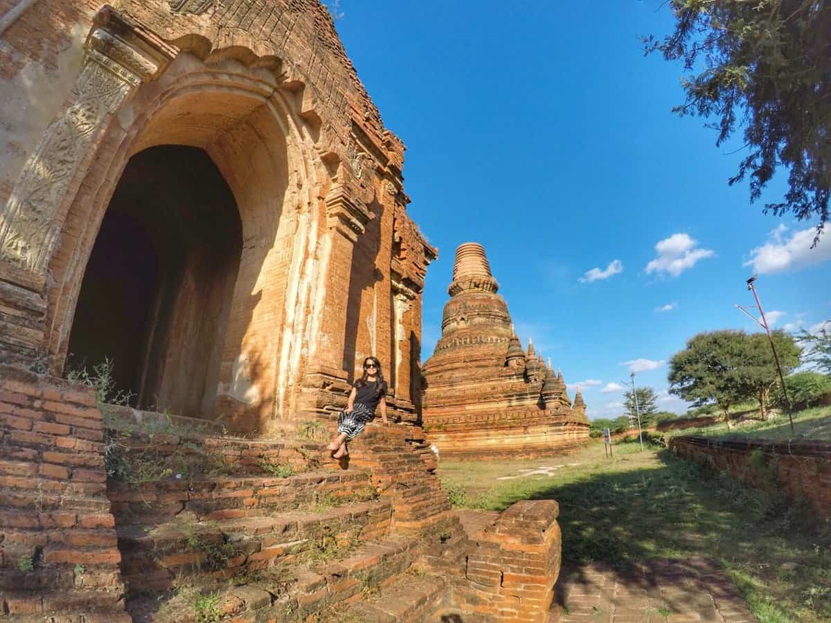 Ancient temple ruins in Bagan, Myanmar, with a person sitting on stone steps in the foreground.