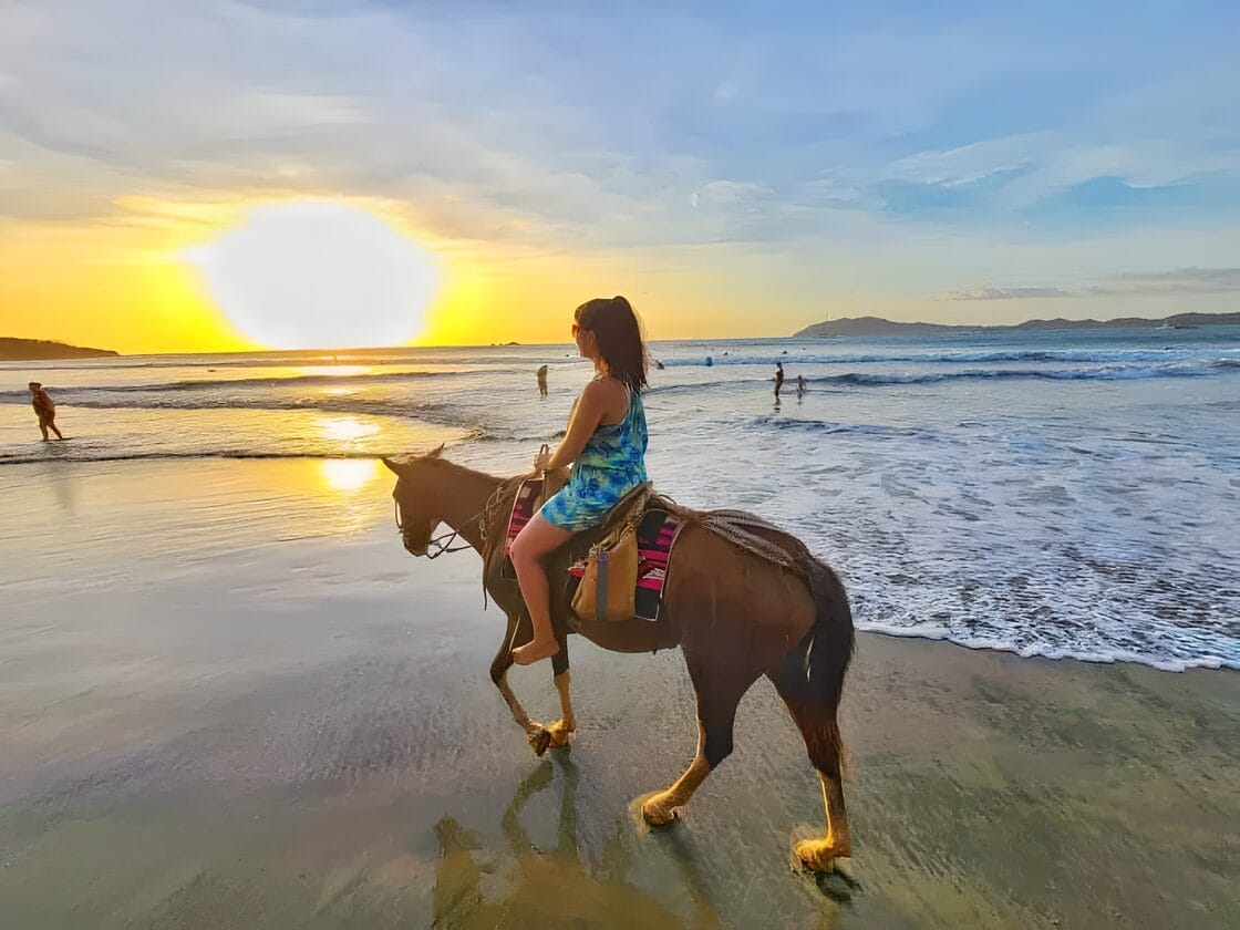 Horseback riding on the beach- Tamarindo must do itinerary Person riding a horse along the beach at sunset in Tamarindo, Costa Rica