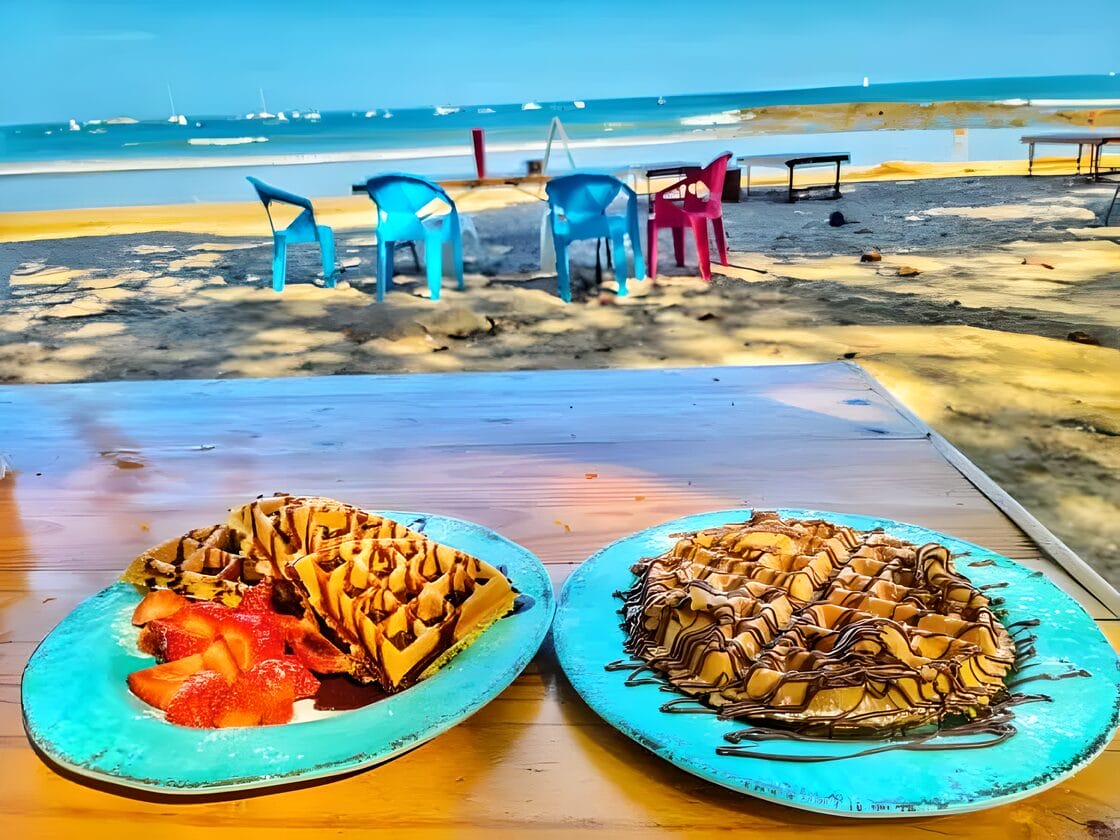 Waffle Monkey in Tamarindo Costa Rica Waffles topped with strawberries and chocolate sauce served on a table with a beach and ocean view at Waffle Monkey in Tamarindo, Costa Rica.