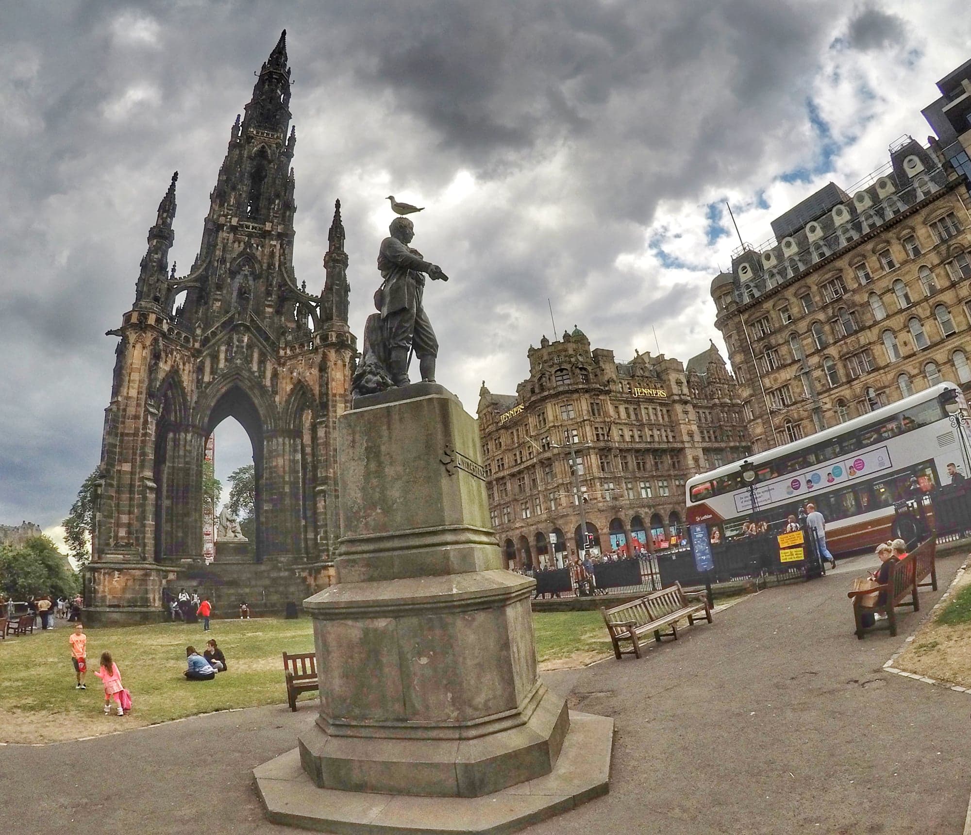 Scott Monument in Edinburgh, Scotland with nearby statue and surrounding buildings on a cloudy day.