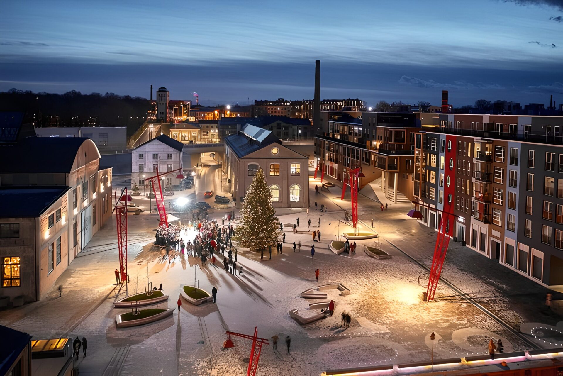 Aerial view of Noblessner seafront quarter in Tallinn, Estonia, during evening. The area is decorated with a large Christmas tree, surrounded by a gathering of people. Modern buildings with illuminated windows and red cranes adorn the snowy scene.