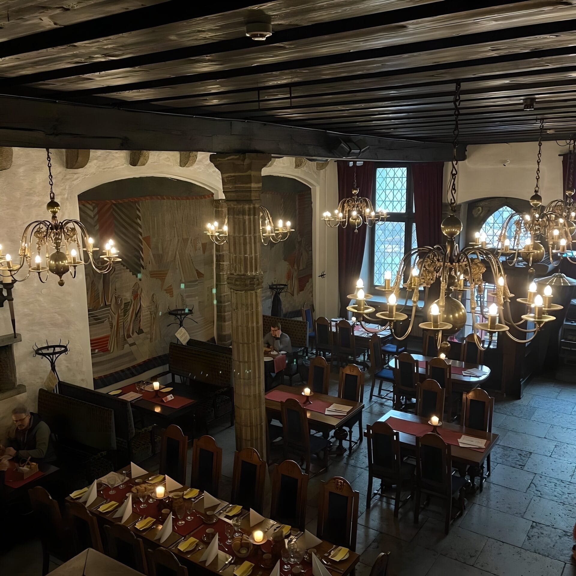 Interior of a traditional restaurant in Tallinn, Estonia, featuring rustic chandeliers, stone pillars, medieval decor, and tables set for dining.