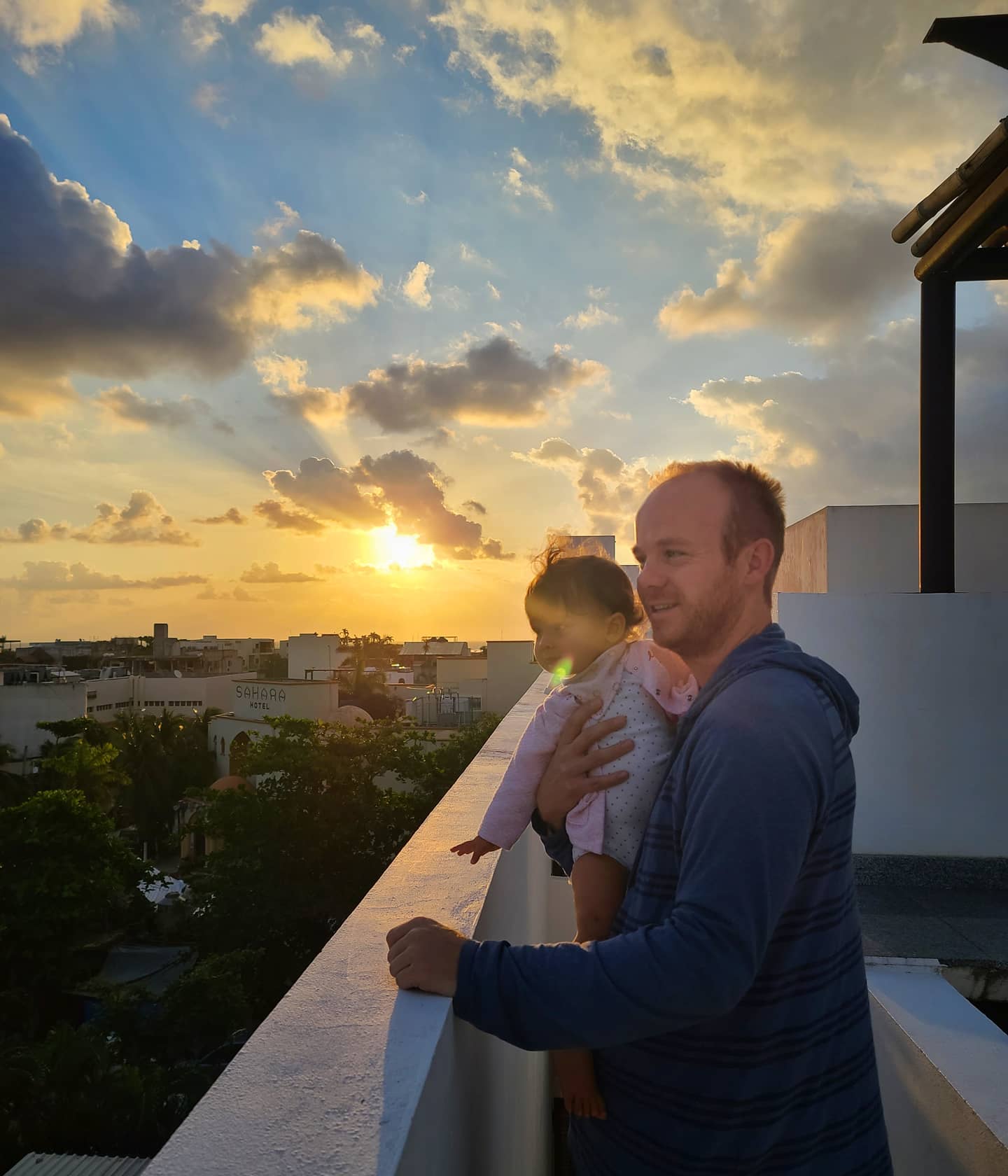 A man holding a baby, both looking at a sunset over the skyline of Playa del Carmen, Riviera Maya, Quintana Roo, Mexico.