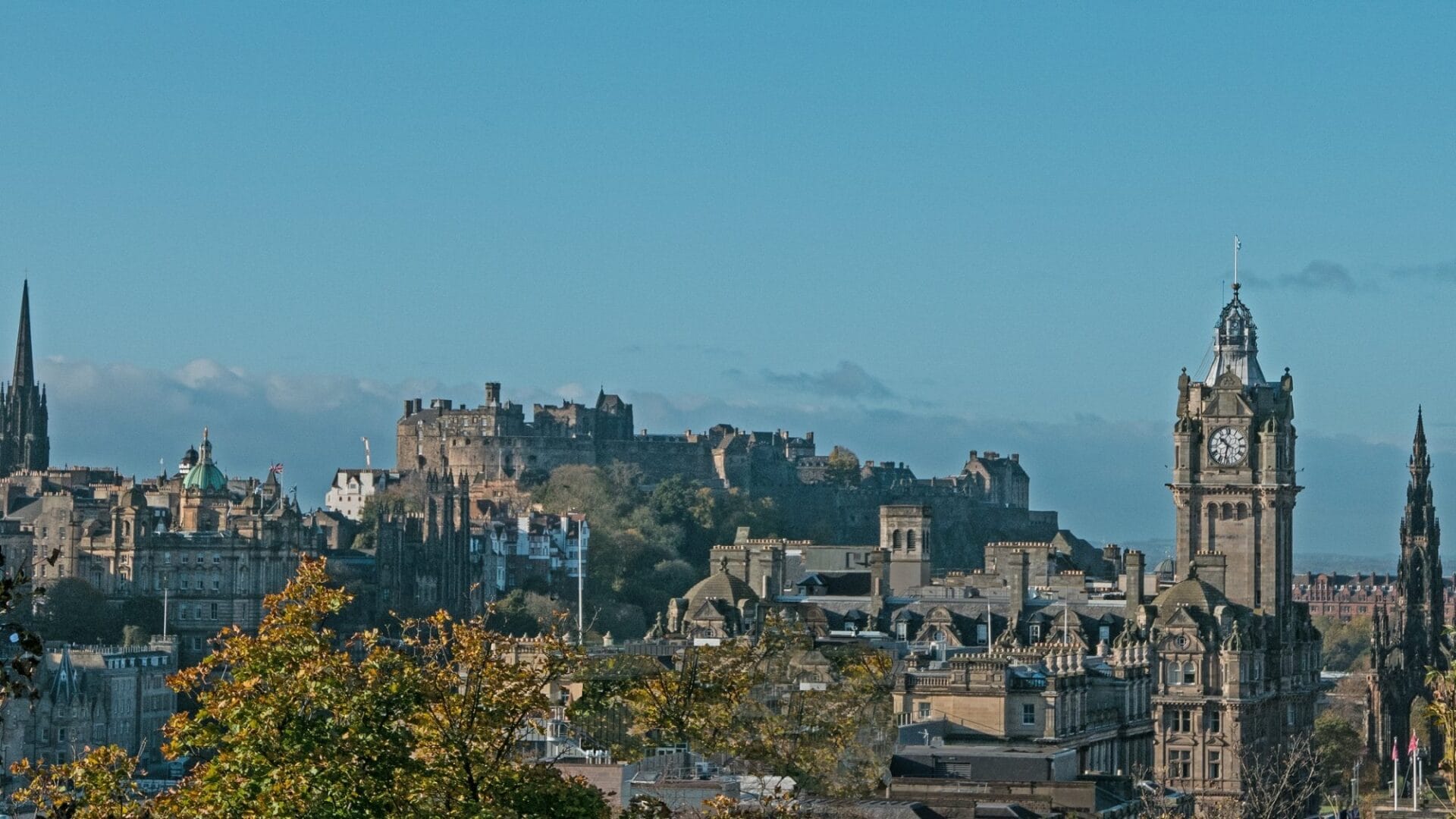 Panoramic view of Edinburgh, Scotland, featuring iconic landmarks including Edinburgh Castle and The Balmoral Hotel with its clock tower.